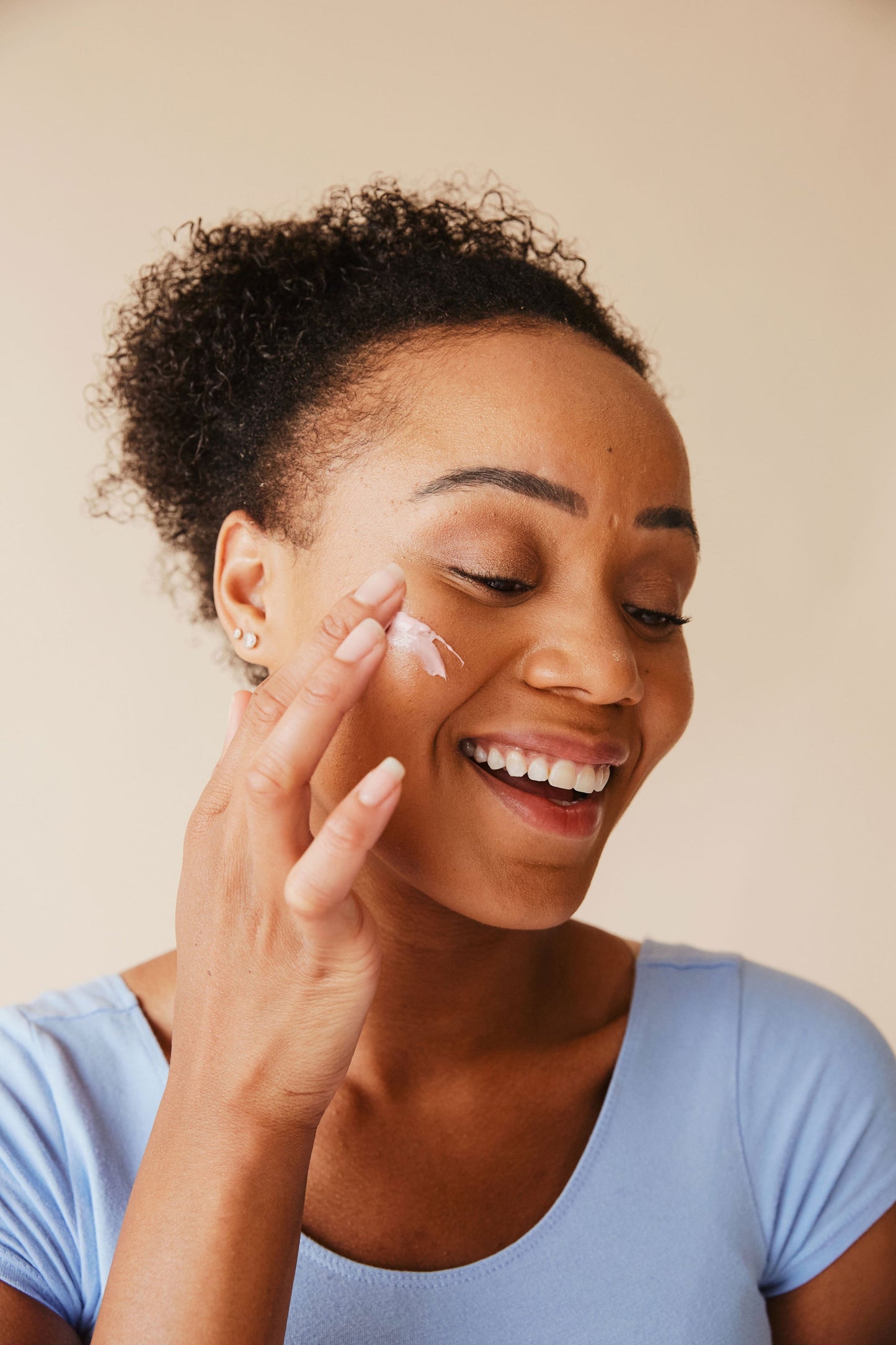 Woman applying cream to her face against a beige background